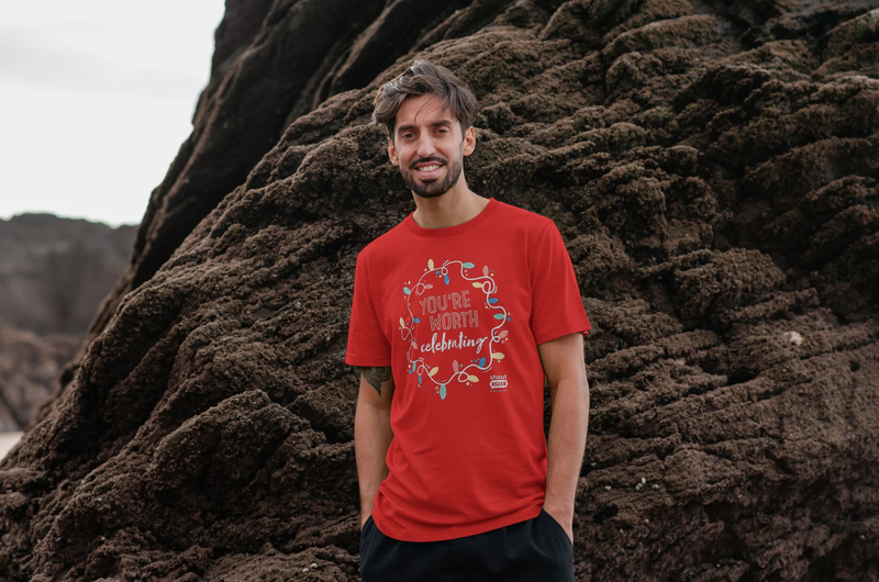 White man standing in front of rocks wearing a red t-shirt that says You're Worth Celebrating